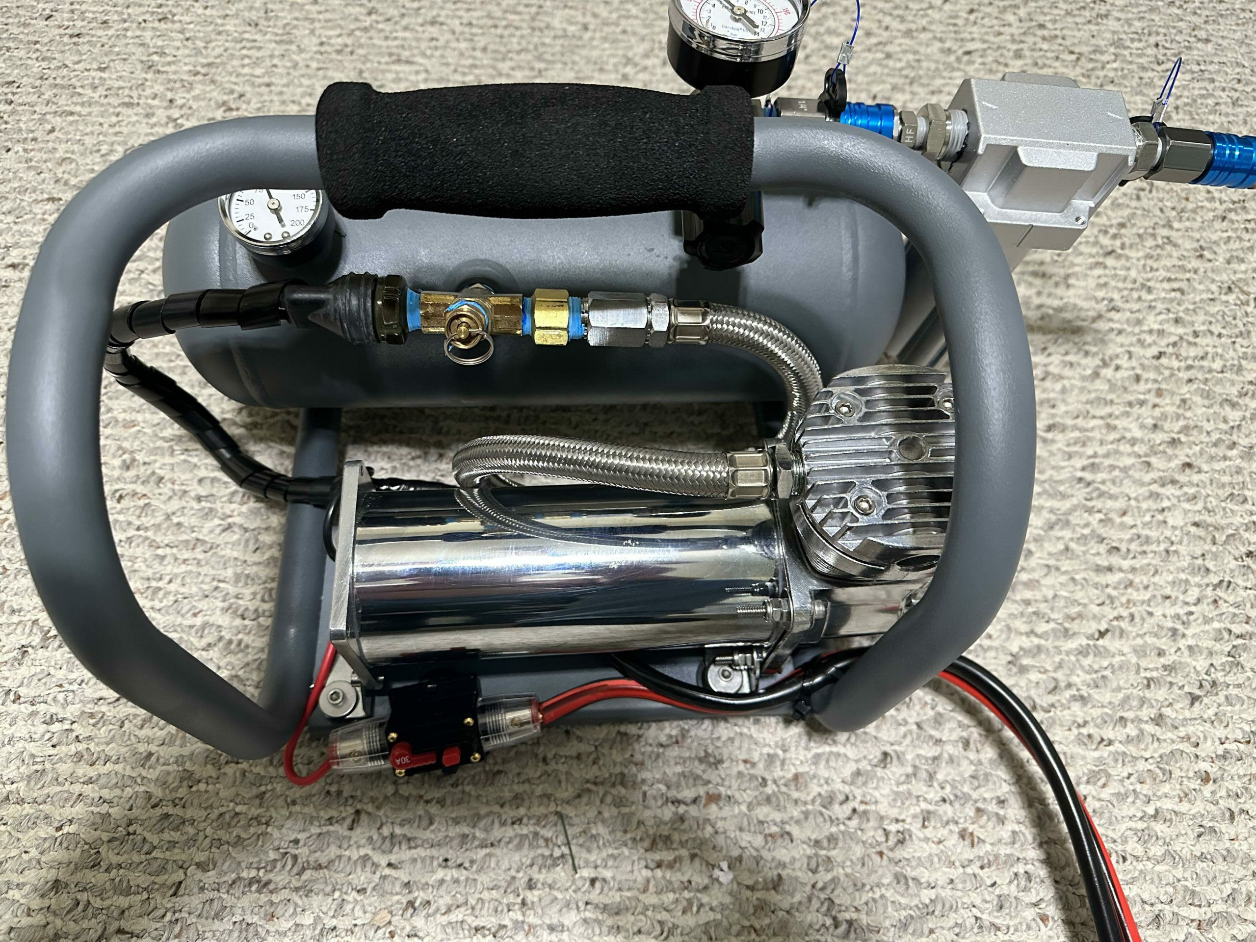 Close-up of a portable air compressor with gauges and hoses on a textured surface.